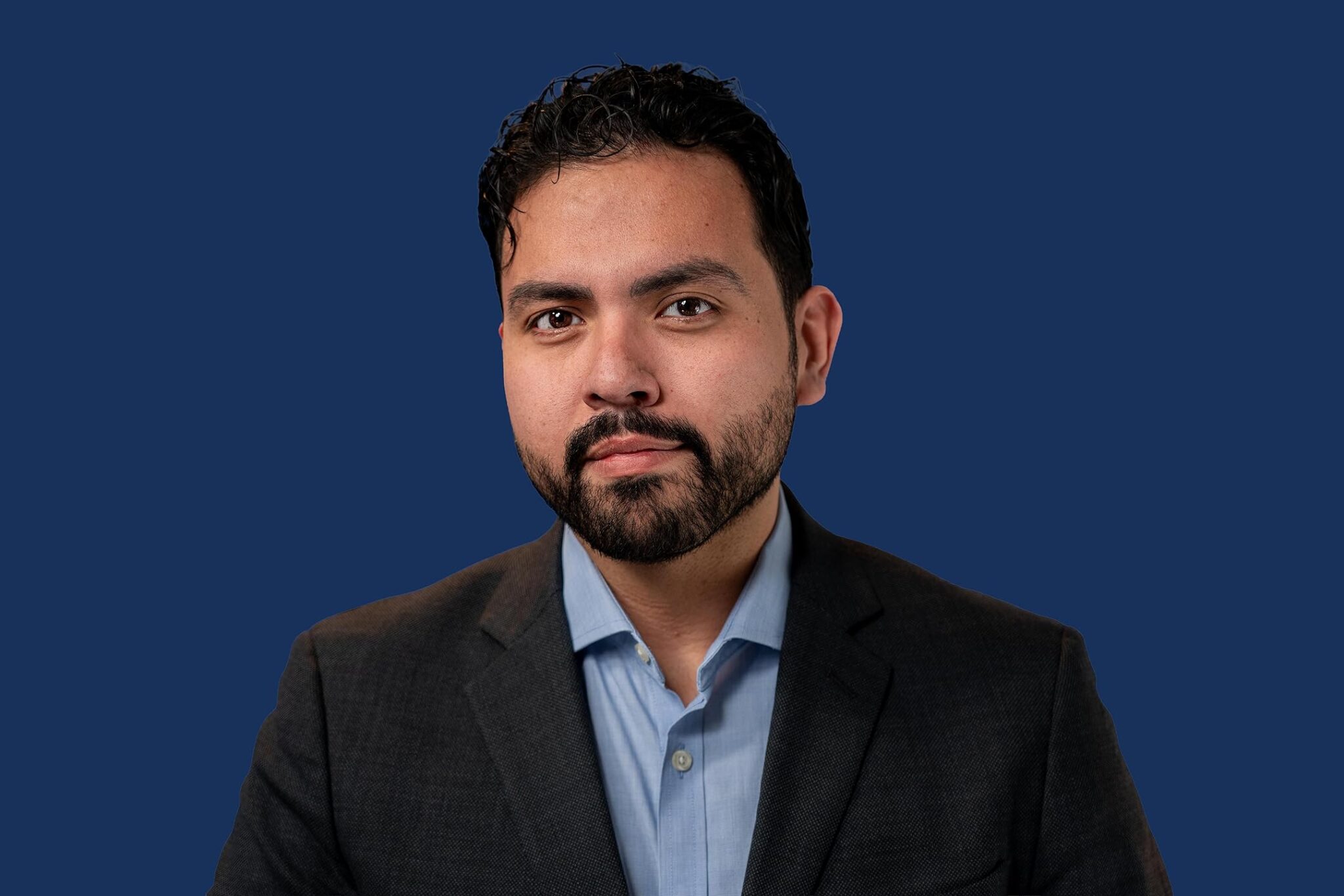 Studio portrait of Jonathan Albarran, confident businessman in a dark suit and light blue shirt, isolated on a deep navy background